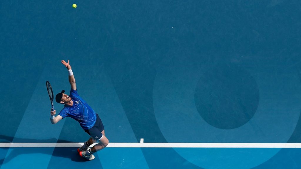 Australian Open Launches NFTs With Free Finals Week Tickets A male tennis player stands at the baseline service a ball. He is at the Australian Open, where they are dropping new 2023 NFTs.