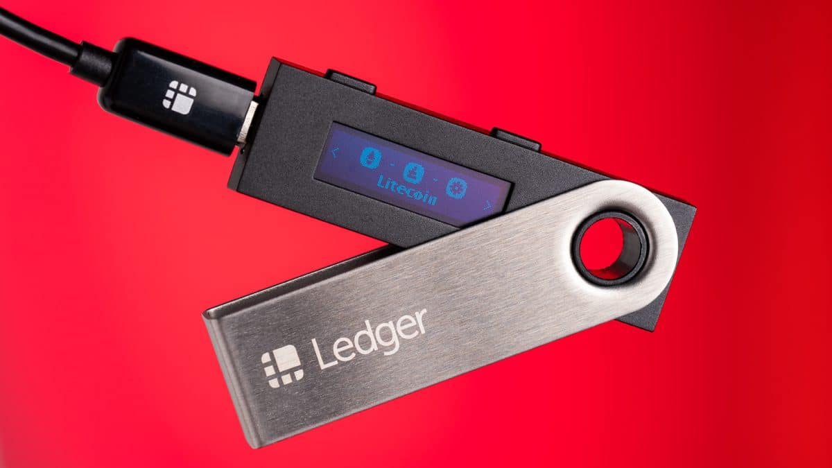 A plugged in Ledger device is pictured against a red background.