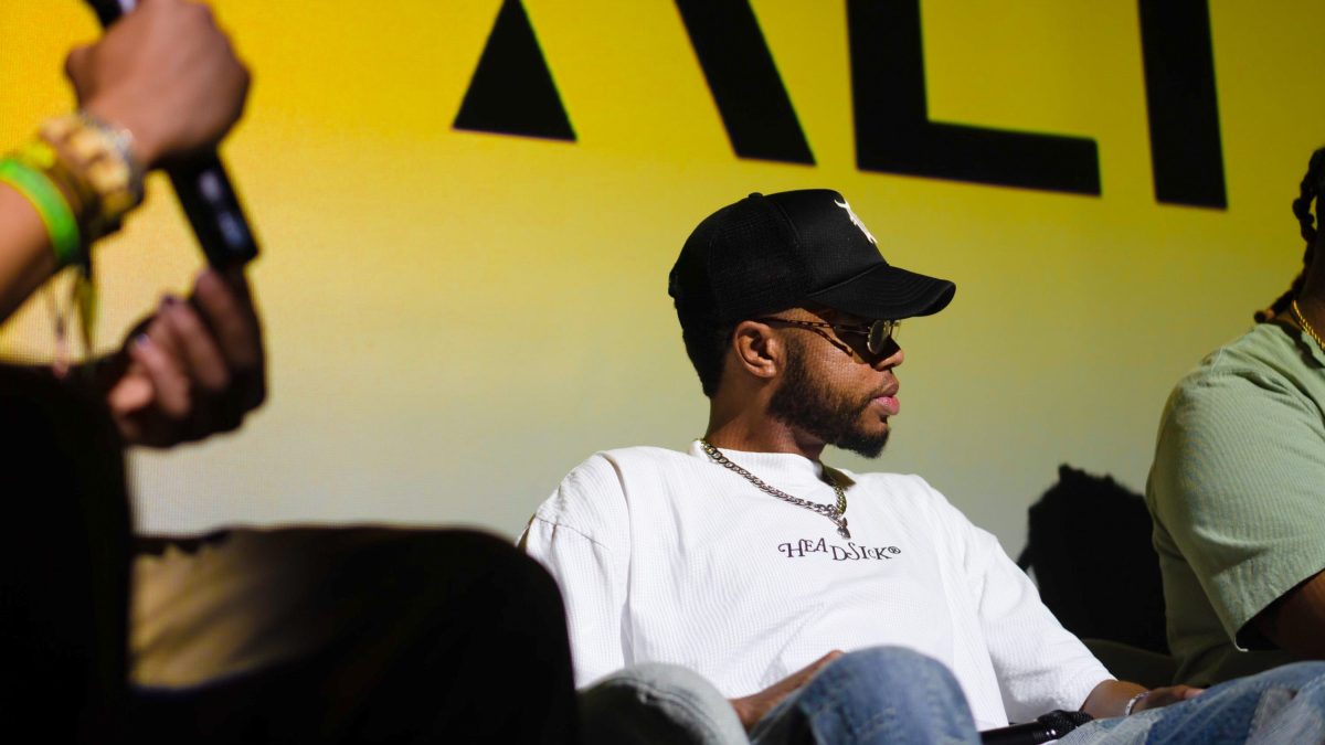 The artist Terrell Jones sits on stage during a panel, wearing a black cap and white shirt.